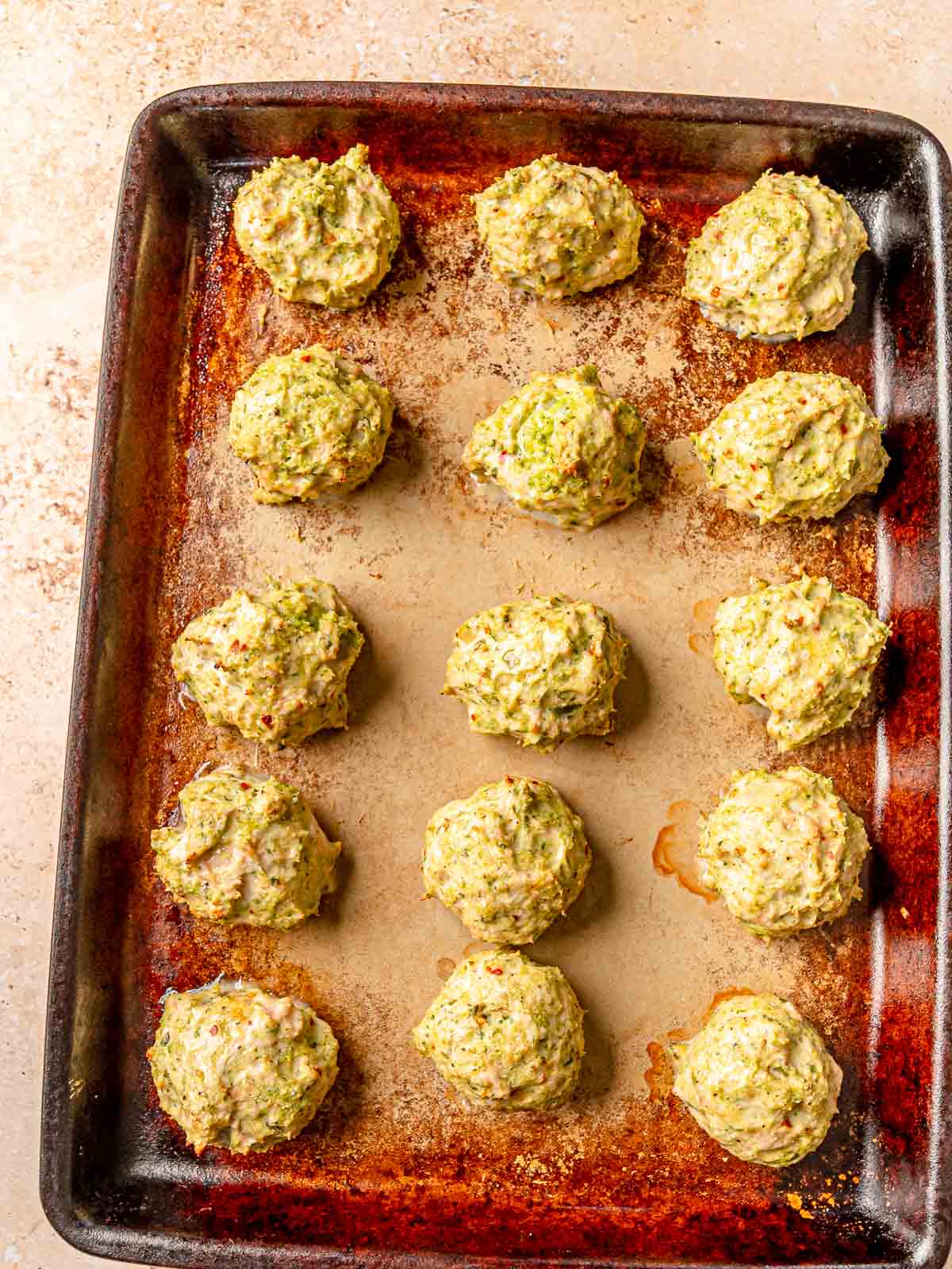 Baked pesto chicken meatballs with golden-brown edges on a baking sheet.