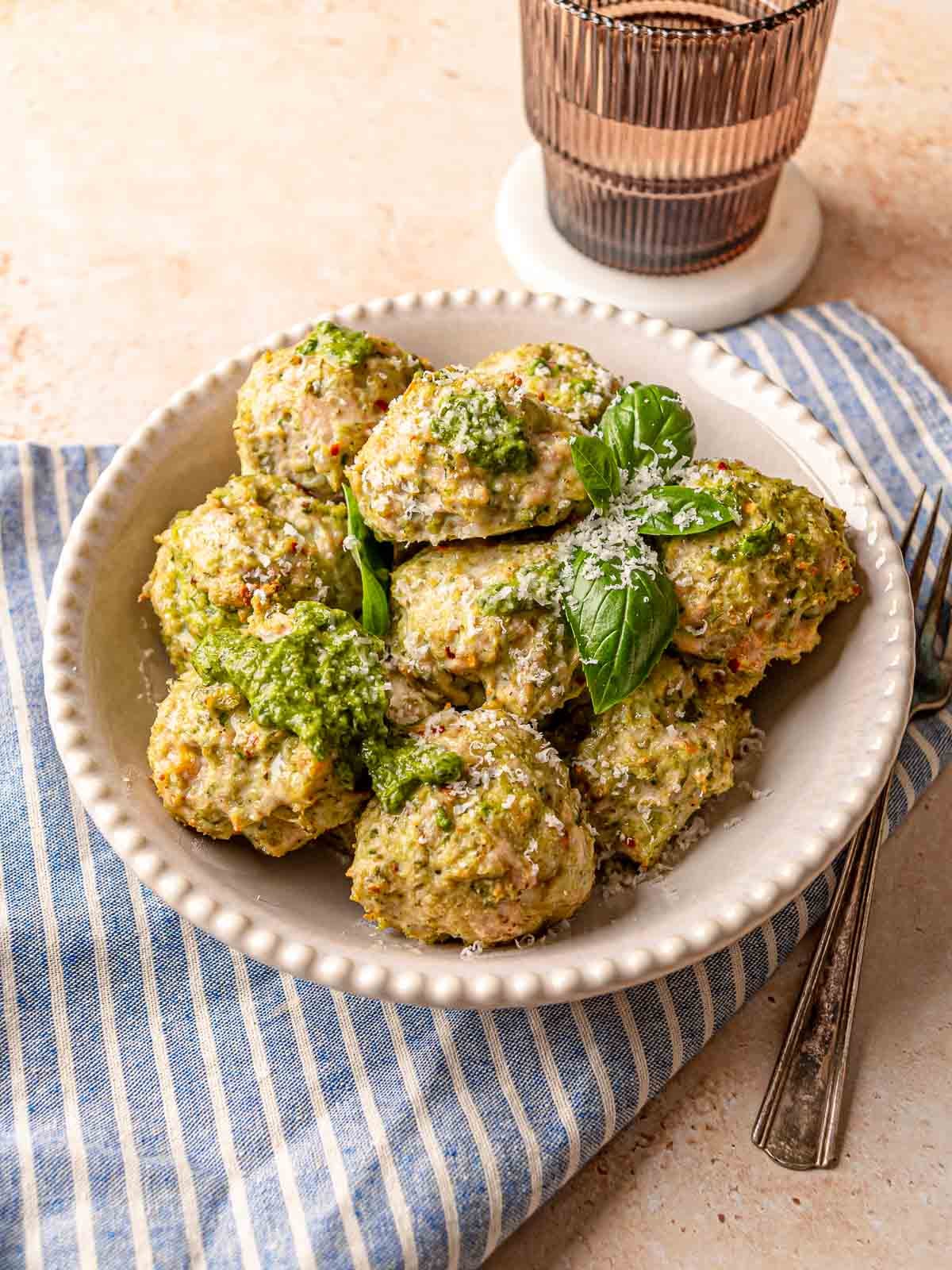 Plate of pesto chicken meatballs garnished with Parmesan cheese and basil next to a glass.