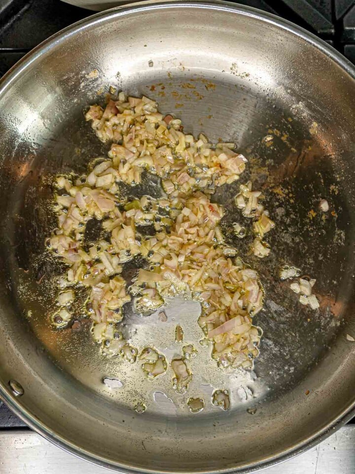 Diced shallots cooking in rendered guanciale fat in a skillet.