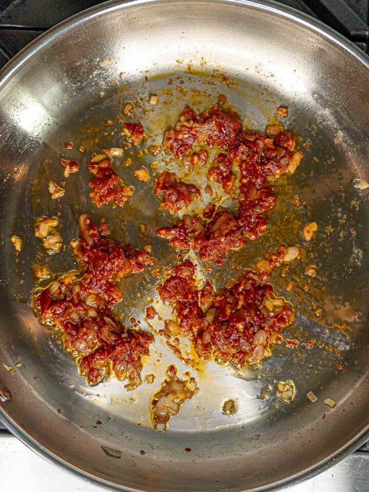 Tomato paste added to the skillet with caramelized shallots and guanciale.