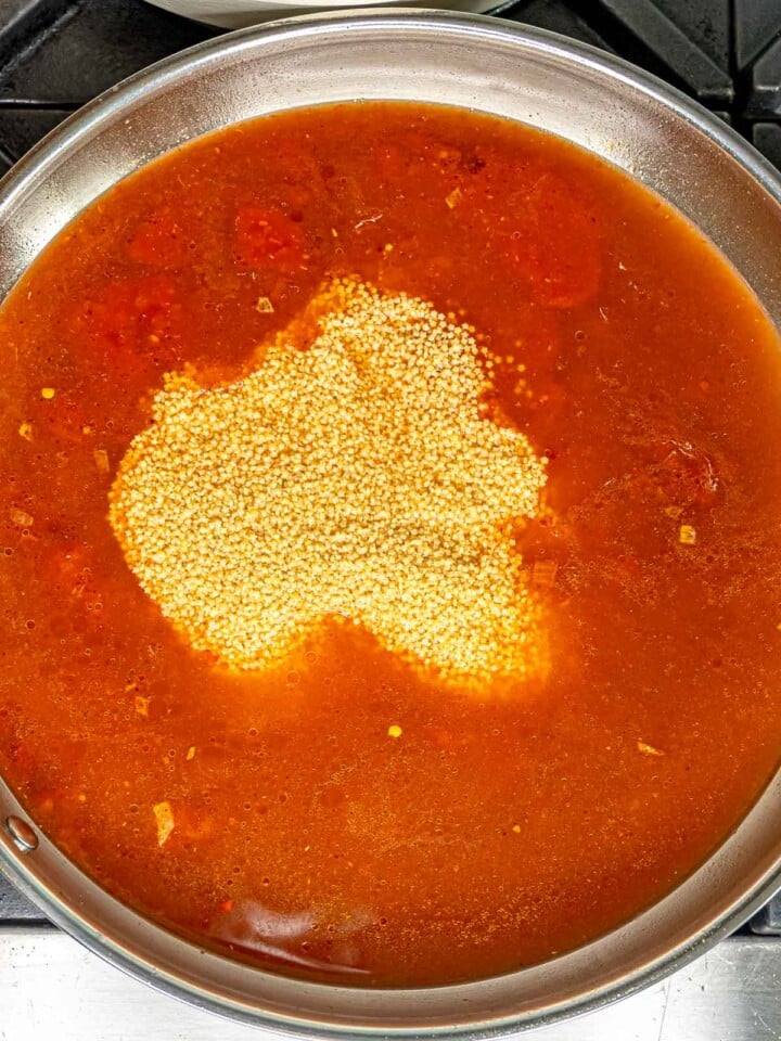 Pastina pasta added to bright red tomato broth in the skillet.