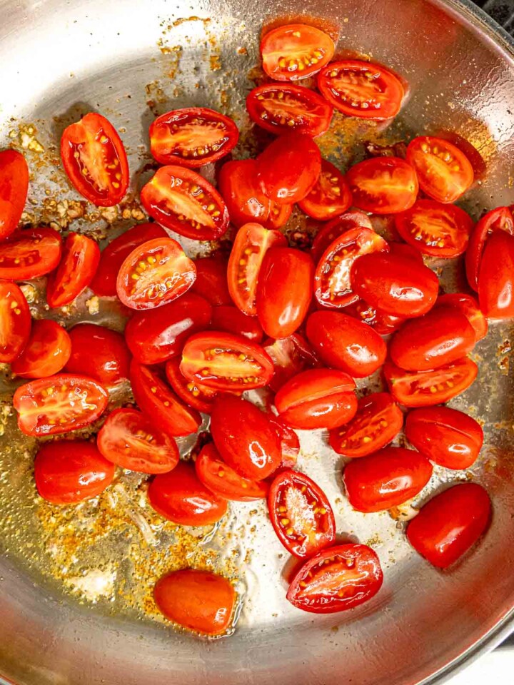 Halved cherry tomatoes cooking in garlic and oil after removing chicken from skillet.