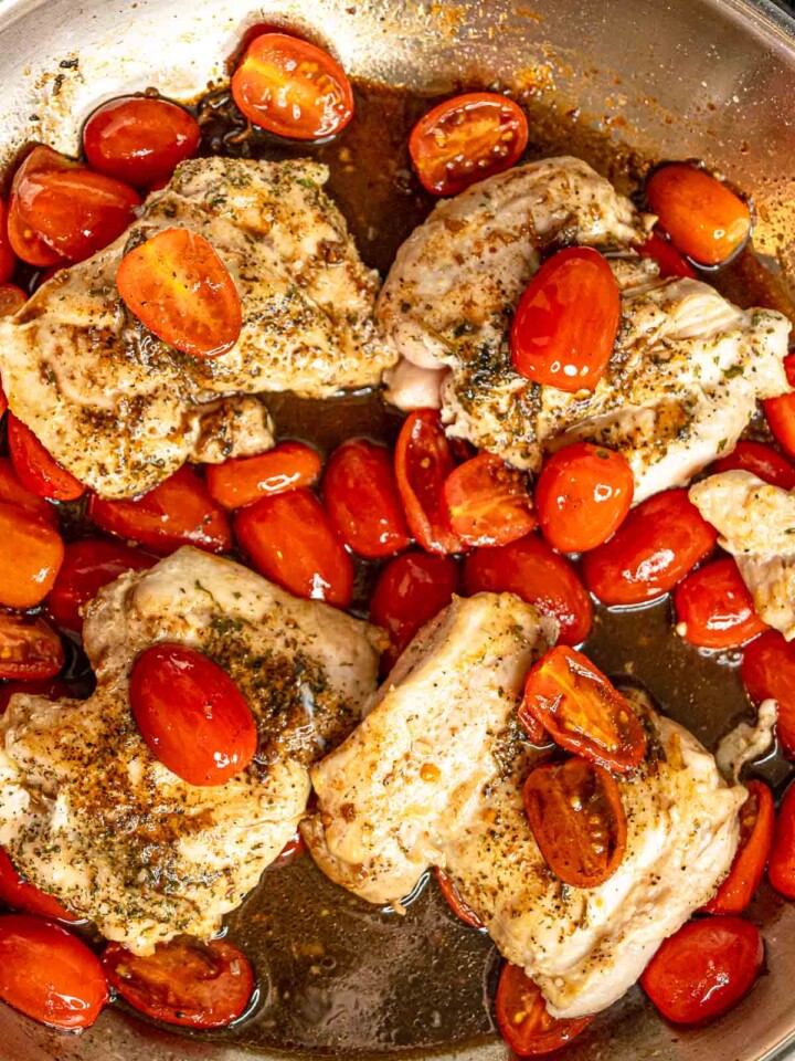 Seared chicken thighs returned to skillet with blistered cherry tomatoes.