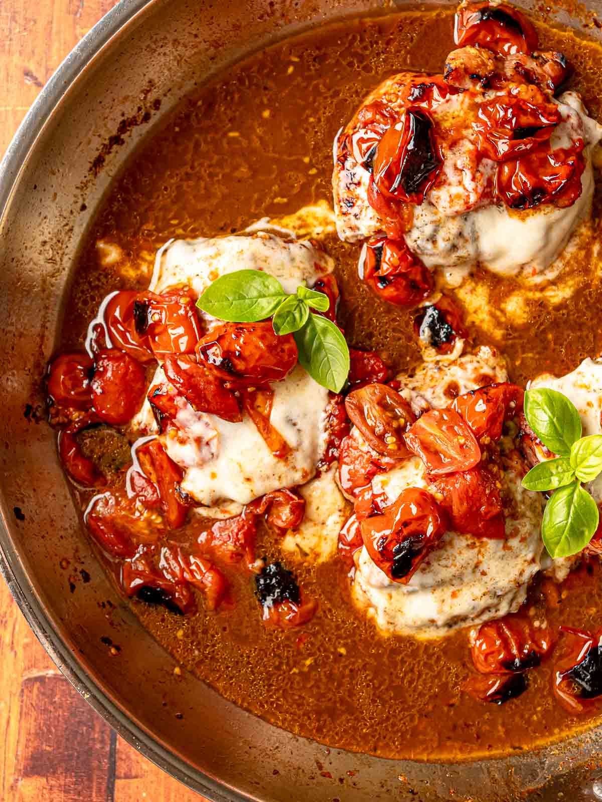 Finished caprese chicken in skillet with mozzarella, balsamic glaze, and basil leaves.