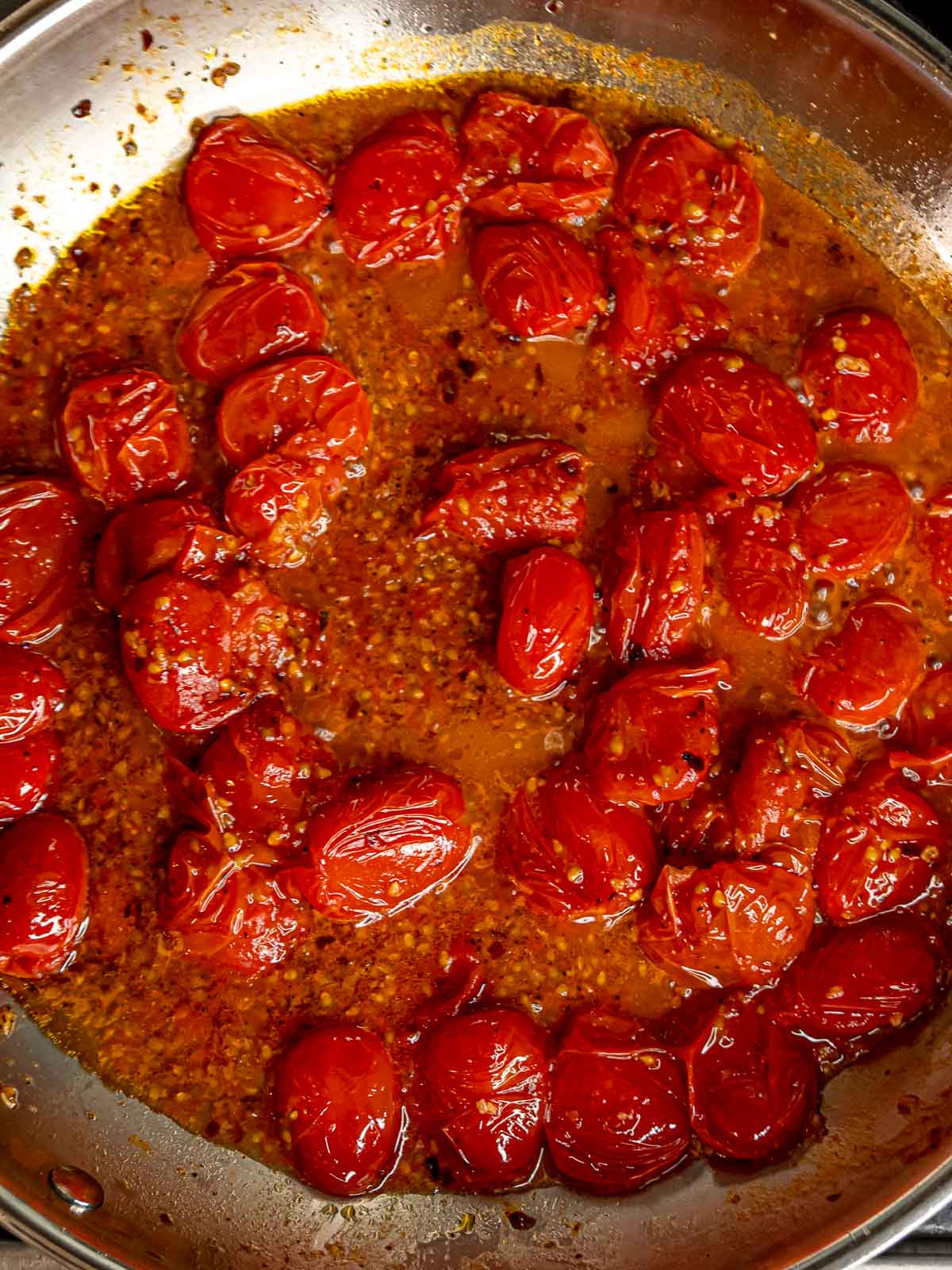 Cherry tomatoes breaking down and releasing juices into glossy garlic-infused sauce.