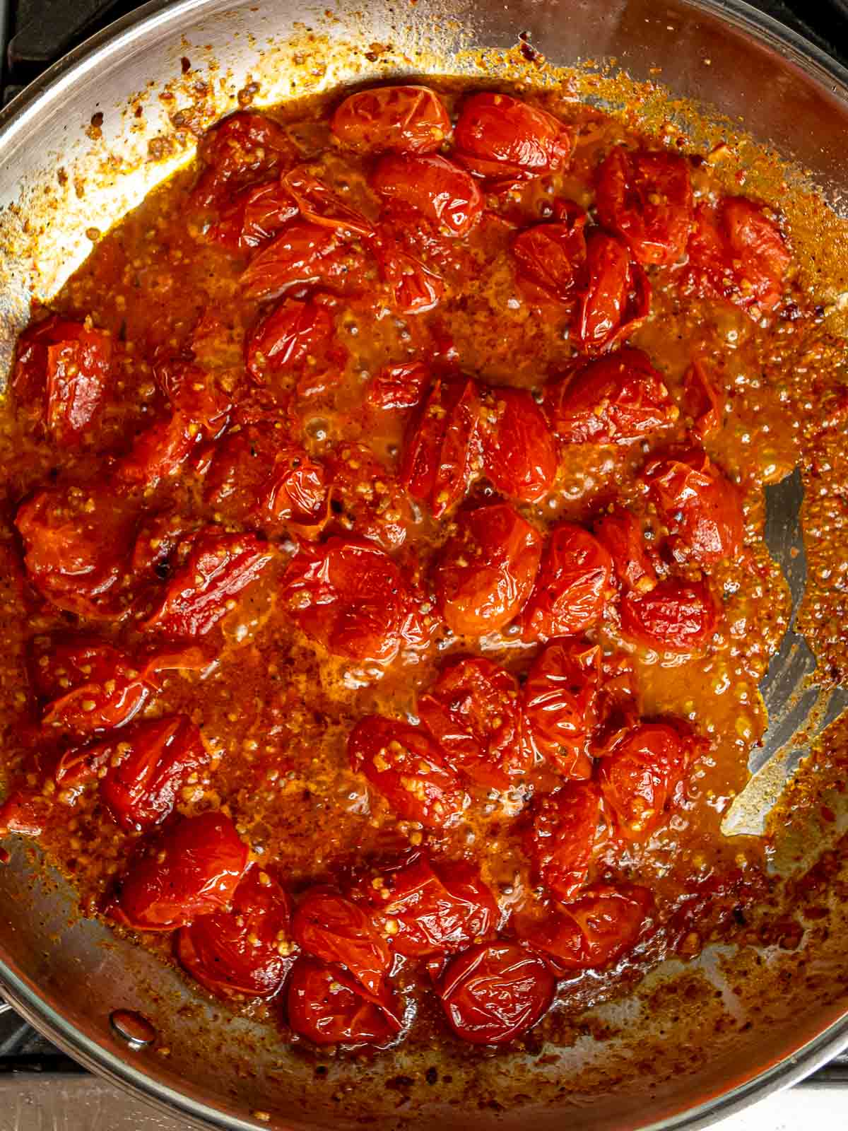 Burst cherry tomatoes simmering in rich tomato sauce with visible garlic and herbs.
