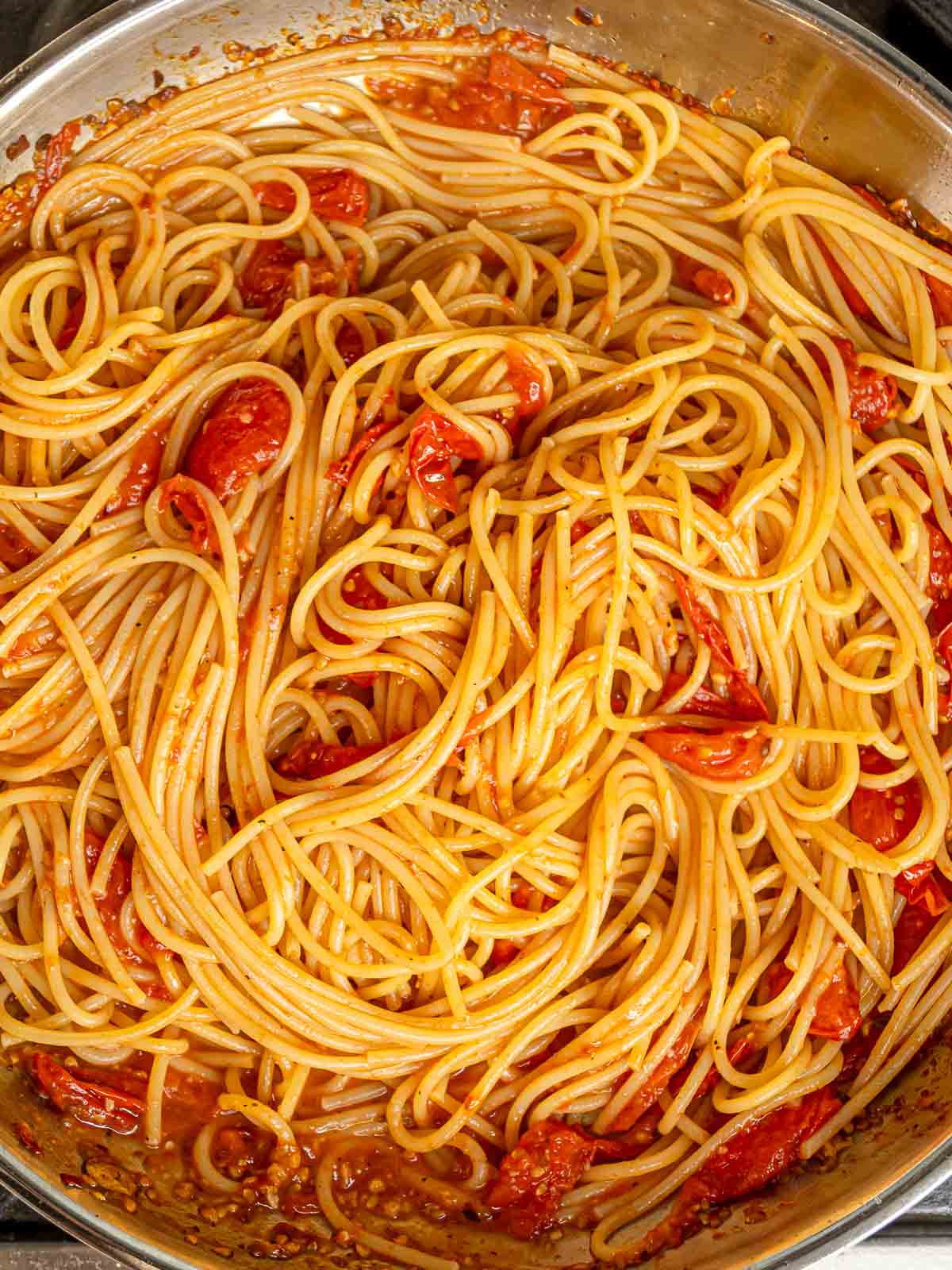 Cooked spaghetti tossed in cherry tomato sauce with burst tomatoes throughout.