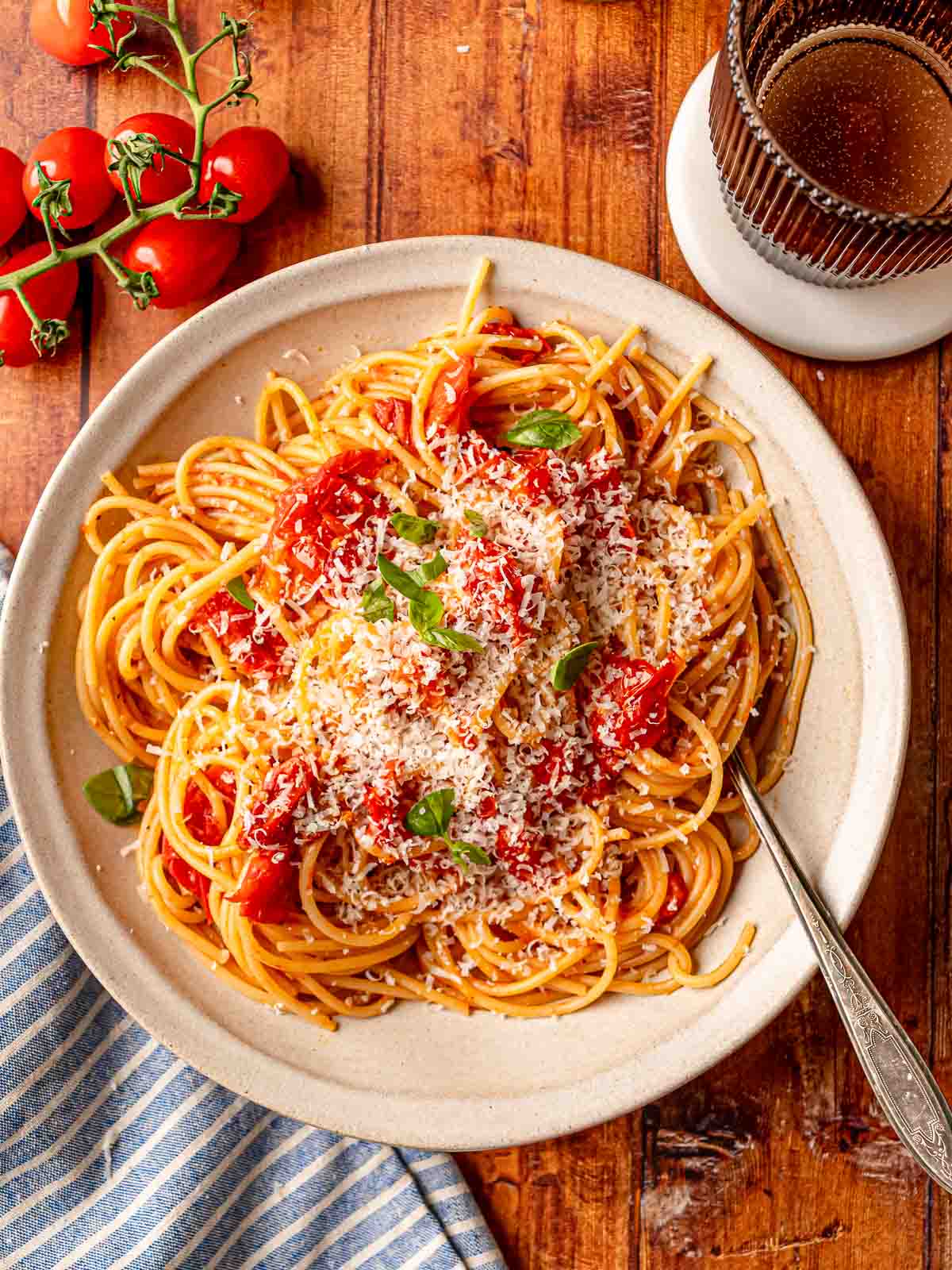 Bowl of spaghetti with cherry tomato sauce topped with grated Parmesan and fresh basil.