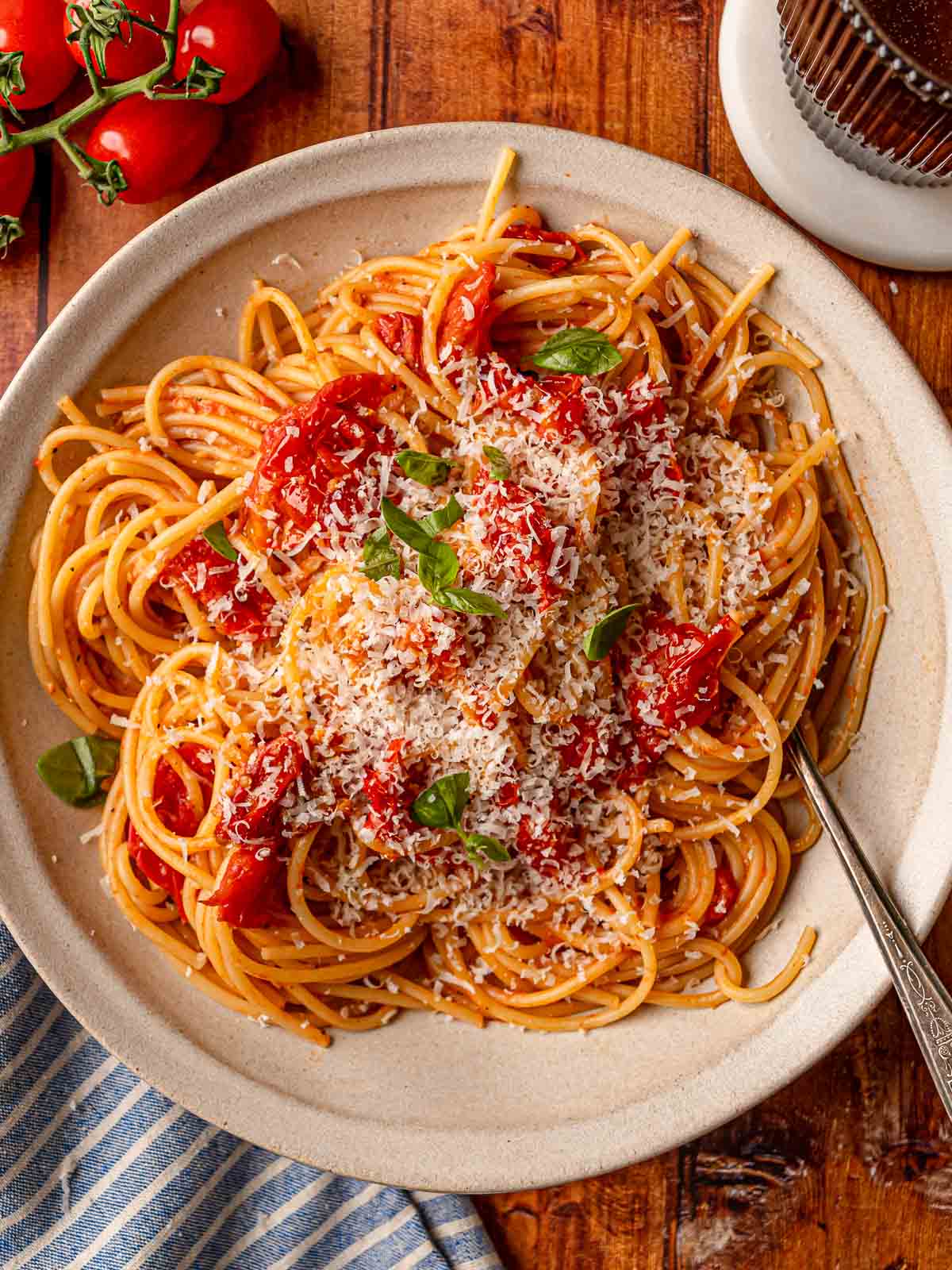 Spaghetti in cherry tomato sauce garnished with Parmesan cheese and basil leaves in white bowl.
