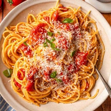 Cherry tomato pasta with grated Parmesan, fresh basil, and burst tomatoes in white serving bowl.