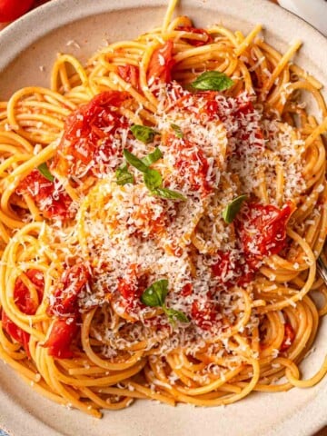 Cherry tomato pasta with grated Parmesan, fresh basil, and burst tomatoes in white serving bowl.
