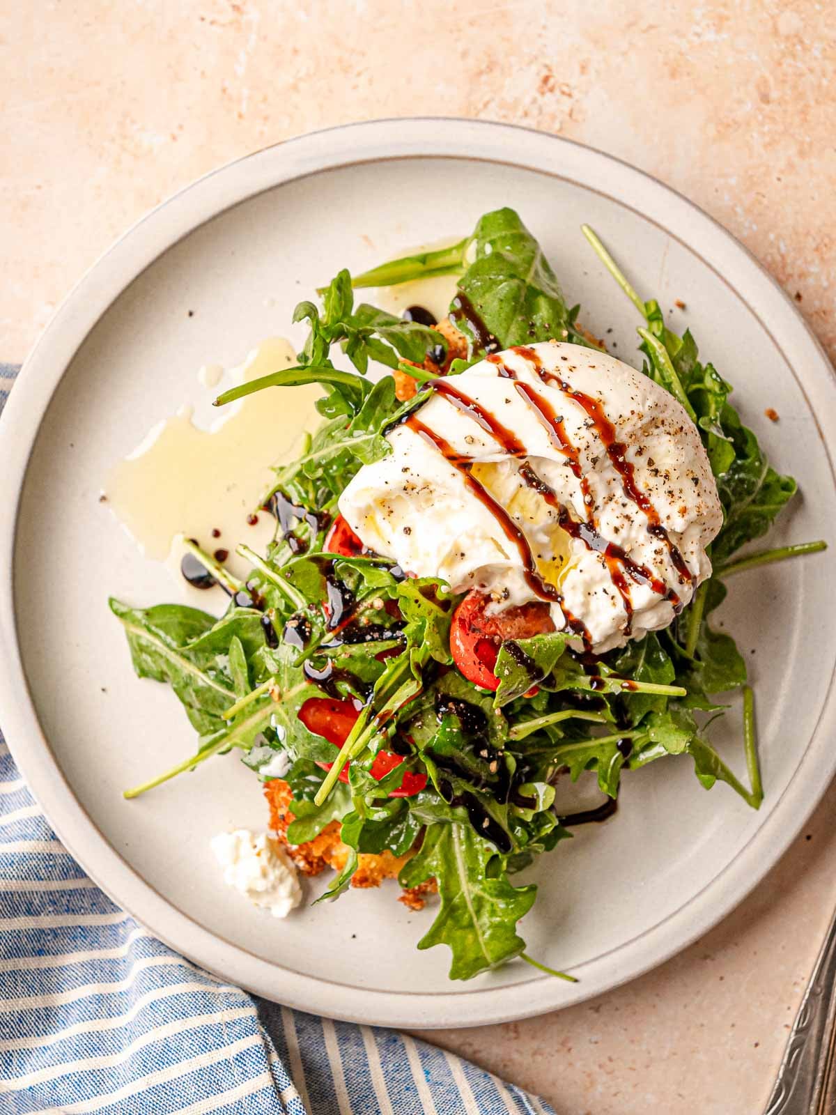 Chicken milanese with arugula, tomatoes, burrata, and balsamic glaze drizzle on white plate.