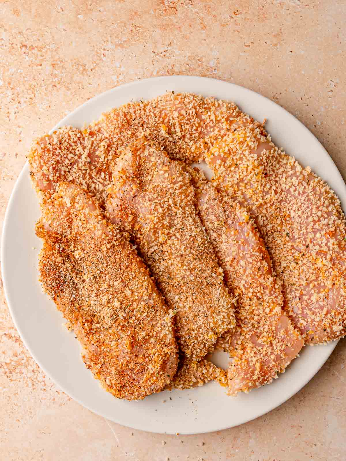 Three breaded chicken cutlets coated in panko breadcrumbs ready for frying.