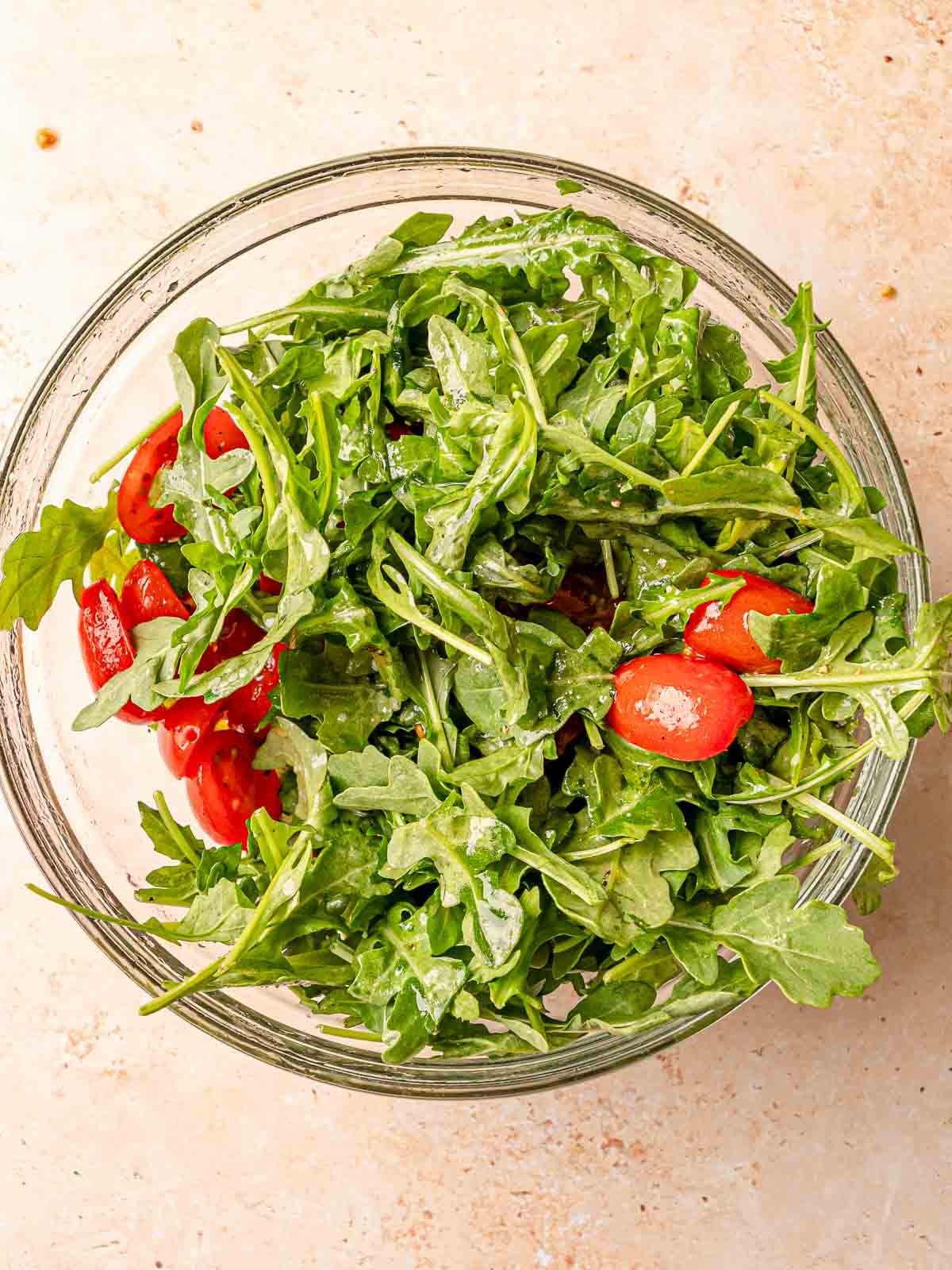 Fresh arugula and halved cherry tomatoes tossed together in glass bowl.