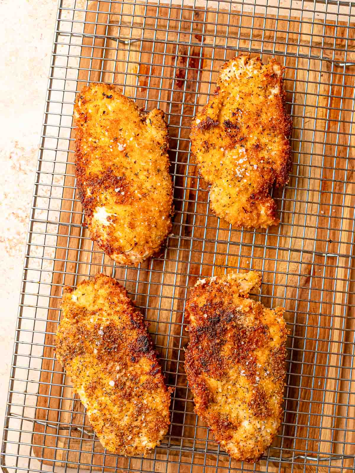 Four golden-brown chicken milanese cutlets resting on wire cooling rack after frying.