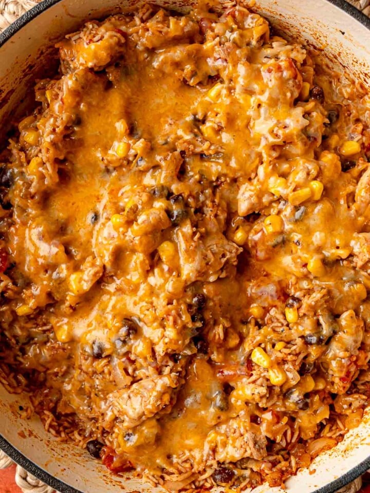 Melted cheese bubbling over chicken, rice, black beans, and corn in skillet.