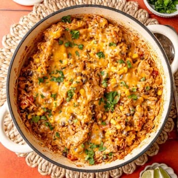 Skillet of cheesy Tex-Mex chicken and rice garnished with cilantro, lime wedges alongside.