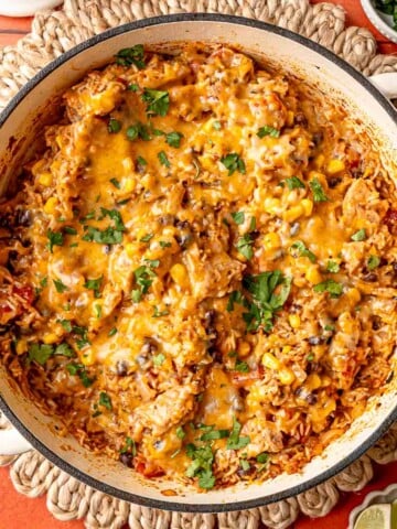 Skillet of cheesy Tex-Mex chicken and rice garnished with cilantro, lime wedges alongside.