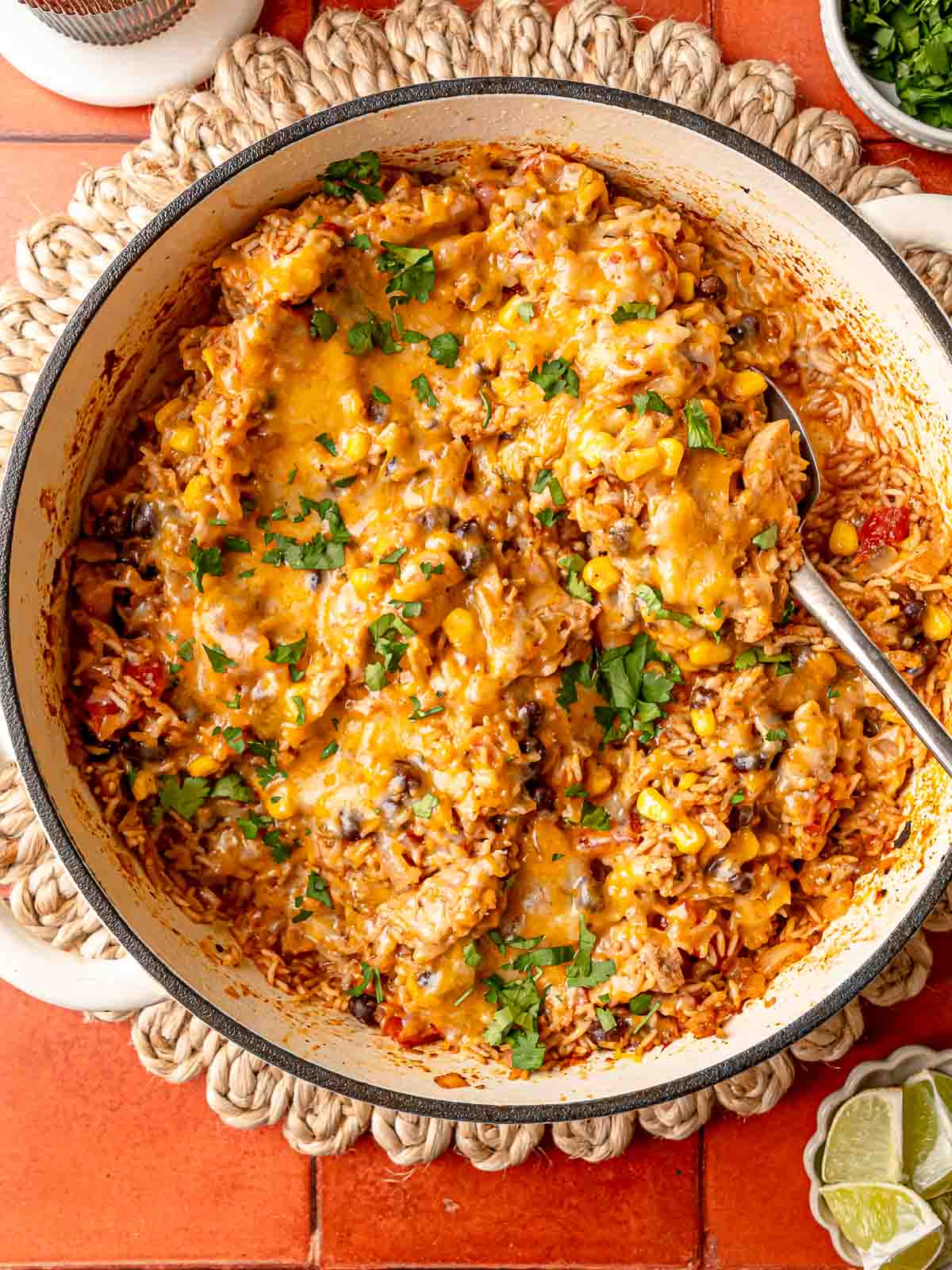 Serving spoon in skillet of melted cheese, chicken, rice, black beans, and corn with cilantro.