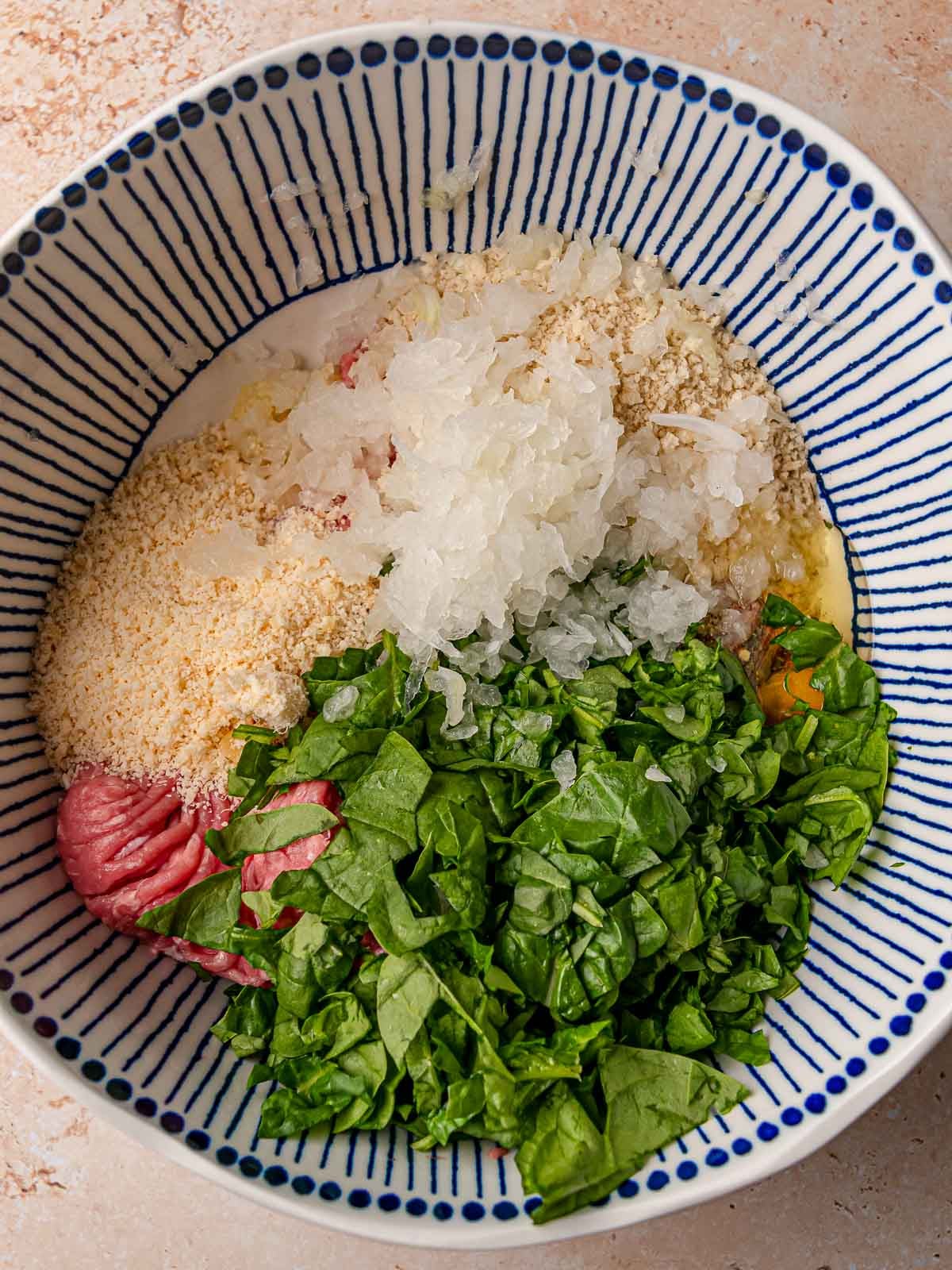 Mixing bowl with ground turkey, chopped spinach, panko breadcrumbs, minced onion, grated parmesan, and egg before mixing.