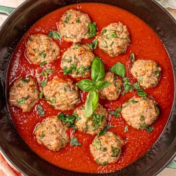 Baked turkey spinach meatballs in marinara sauce topped with fresh basil in cast iron skillet.