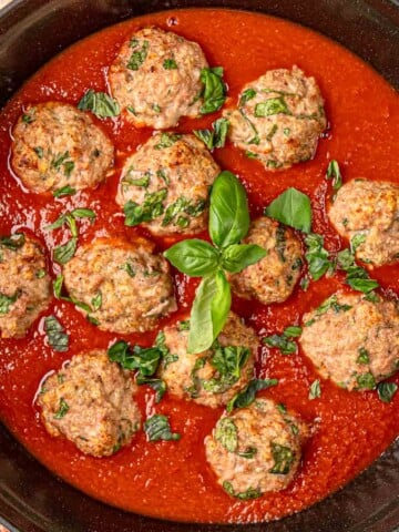 Baked turkey spinach meatballs in marinara sauce topped with fresh basil in cast iron skillet.