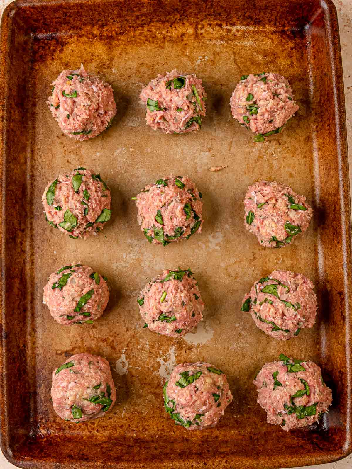 Raw turkey spinach meatballs arranged on a parchment-lined baking sheet before baking.