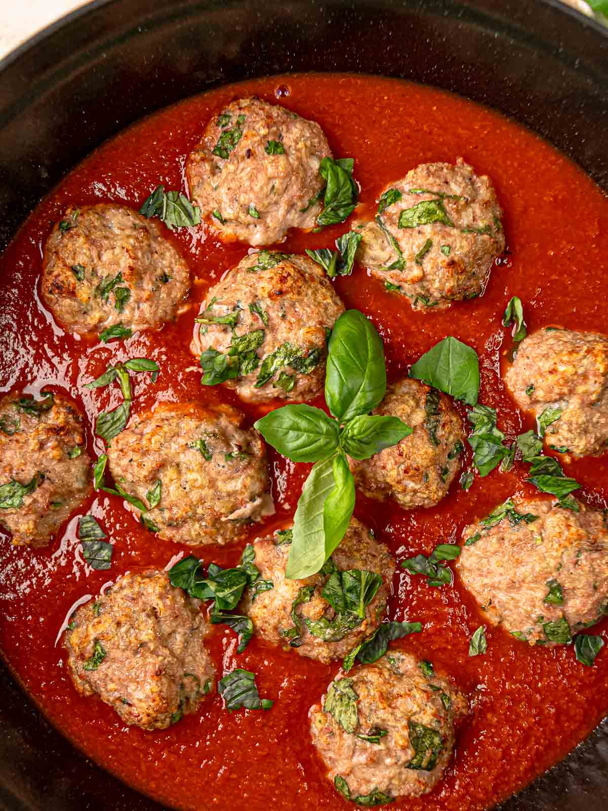 Turkey spinach meatballs in red tomato sauce with fresh basil in a cast iron skillet.