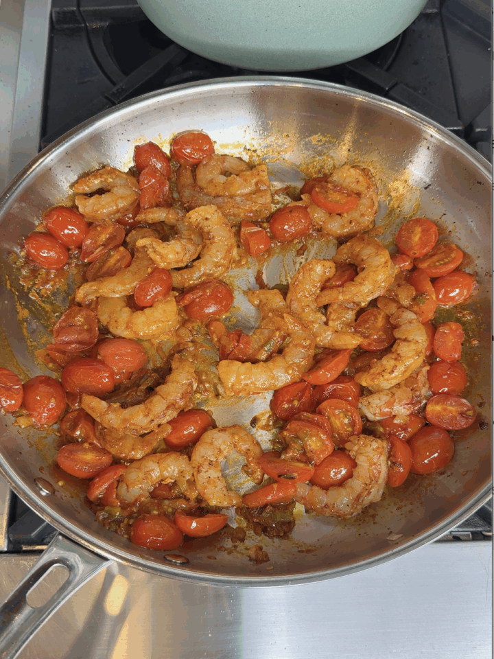 Shrimp and cherry tomatoes cooking in a spicy tomato sauce in a stainless steel skillet.