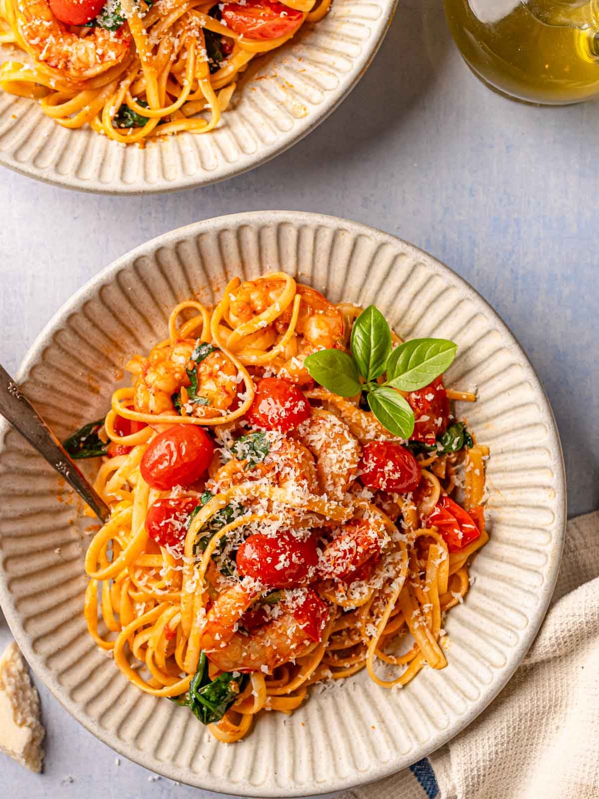Two bowls of spicy tomato shrimp pasta topped with Parmesan and fresh basil.