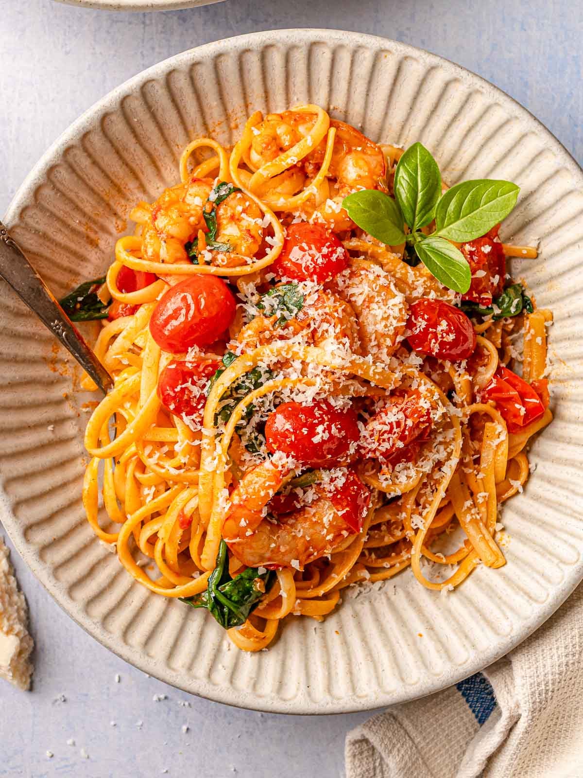 Bowl of spicy tomato shrimp pasta with cherry tomatoes, spinach, Parmesan, and basil.