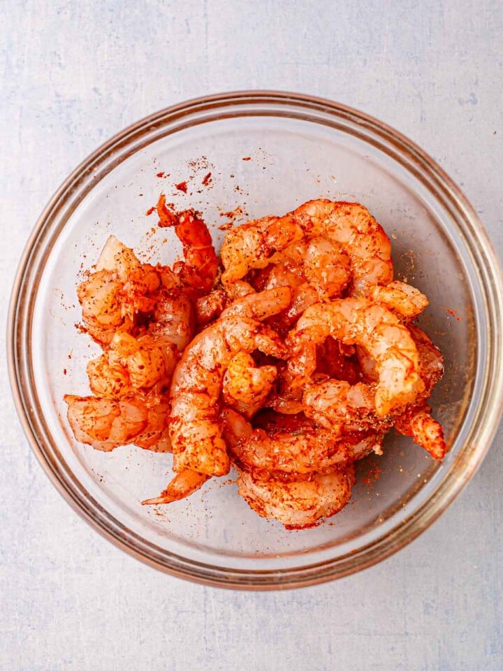 Shrimp tossed with paprika and spices in a clear glass bowl.