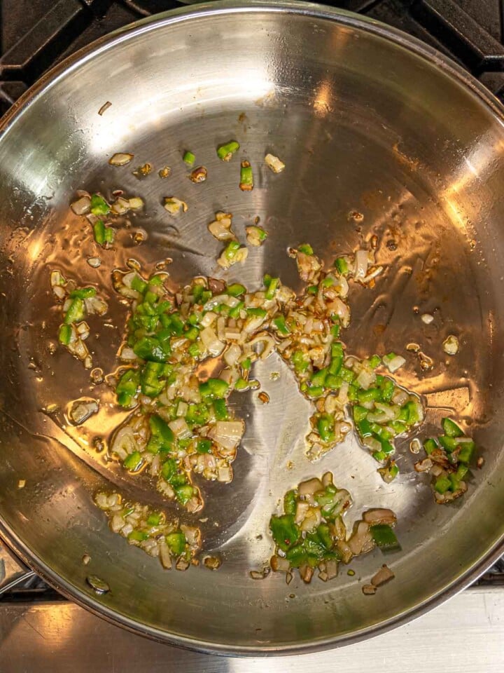 Shallots and pepper cooking in olive oil in a stainless steel skillet.