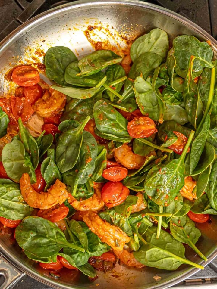 Shrimp, spinach, and blistered tomatoes cooking in a spicy tomato sauce.