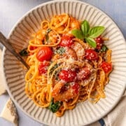 Spicy tomato shrimp pasta served in bowls with Parmesan, basil, and olive oil.
