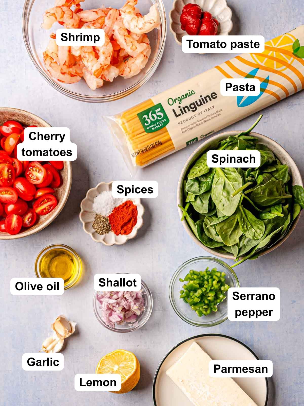 Ingredients for spicy tomato shrimp pasta, including shrimp, linguine, tomatoes, spinach, garlic, lemon, and Parmesan.