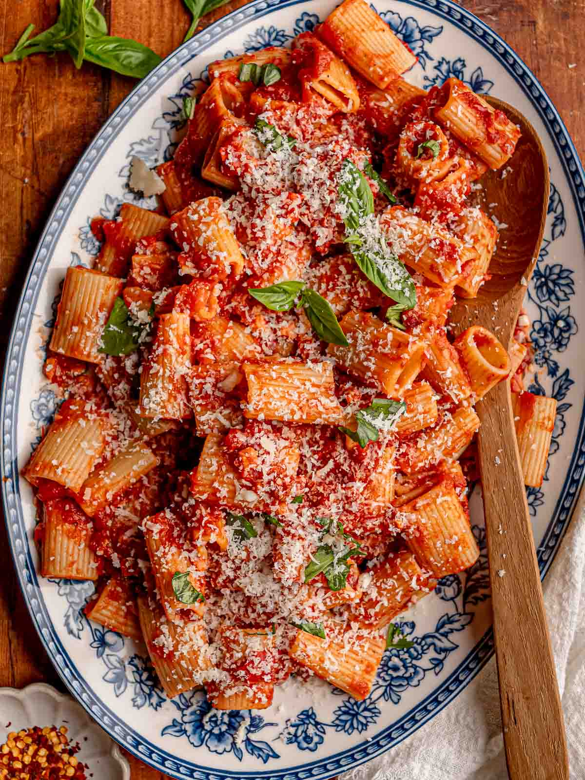 Rigatoni coated in spicy arrabbiata sauce is topped with Parmesan and fresh basil on a blue and white serving platter.