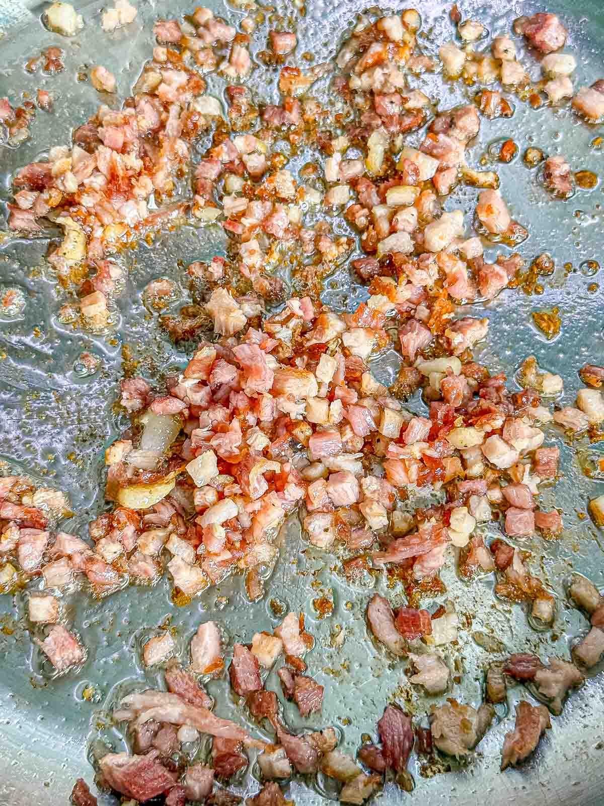 Diced pancetta cooks in a skillet until the fat renders and the edges become golden and crisp.