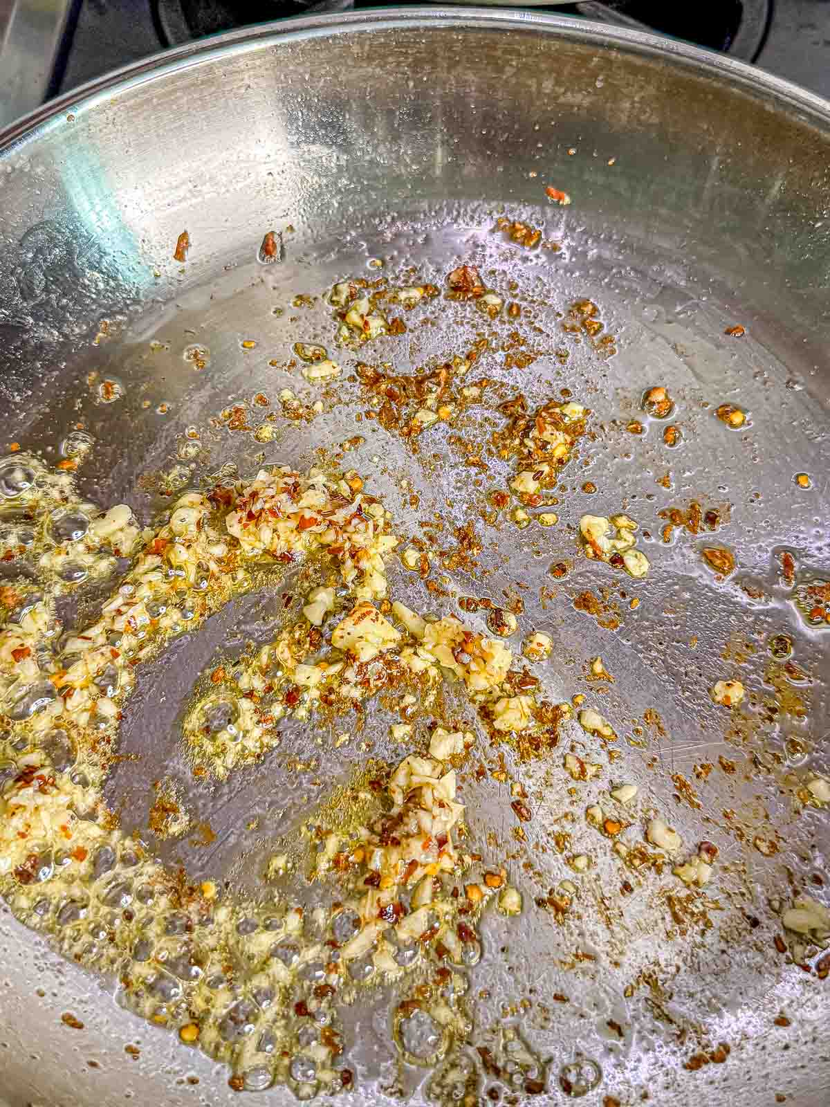 Minced garlic and red pepper flakes cook in the rendered pancetta fat in a large skillet.