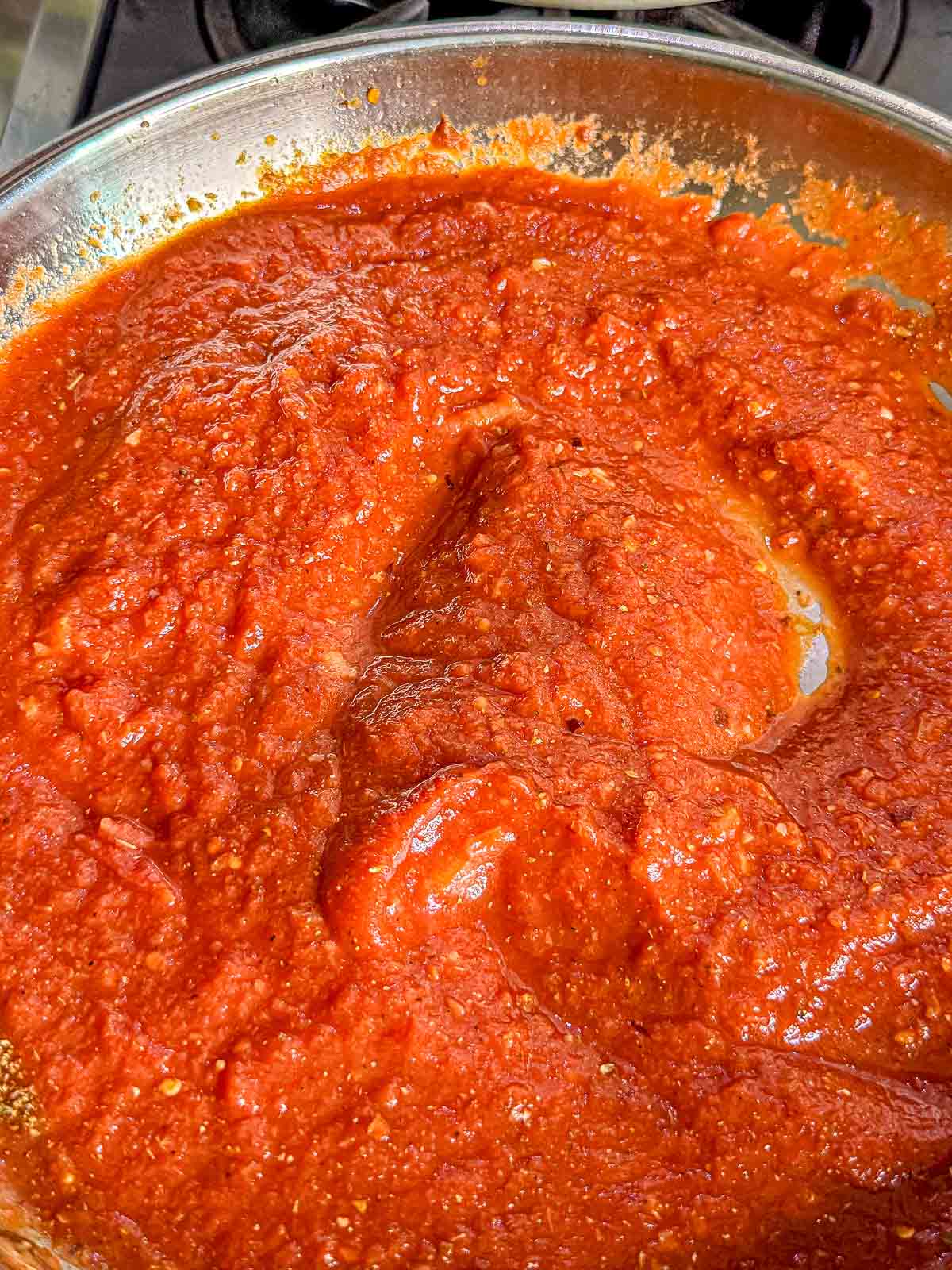 Crushed tomatoes and seasonings are stirred together in a skillet to make a rich red arrabbiata sauce.