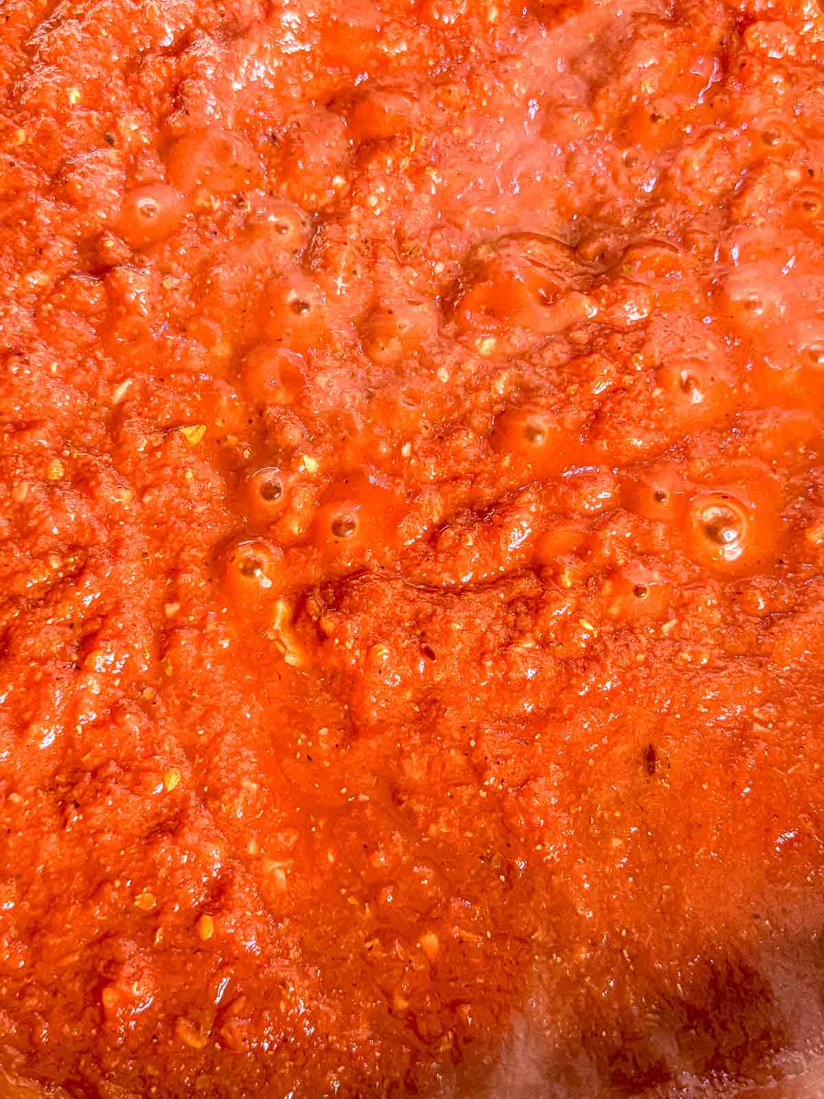 Arrabbiata sauce simmers in a skillet until thickened and bubbling.
