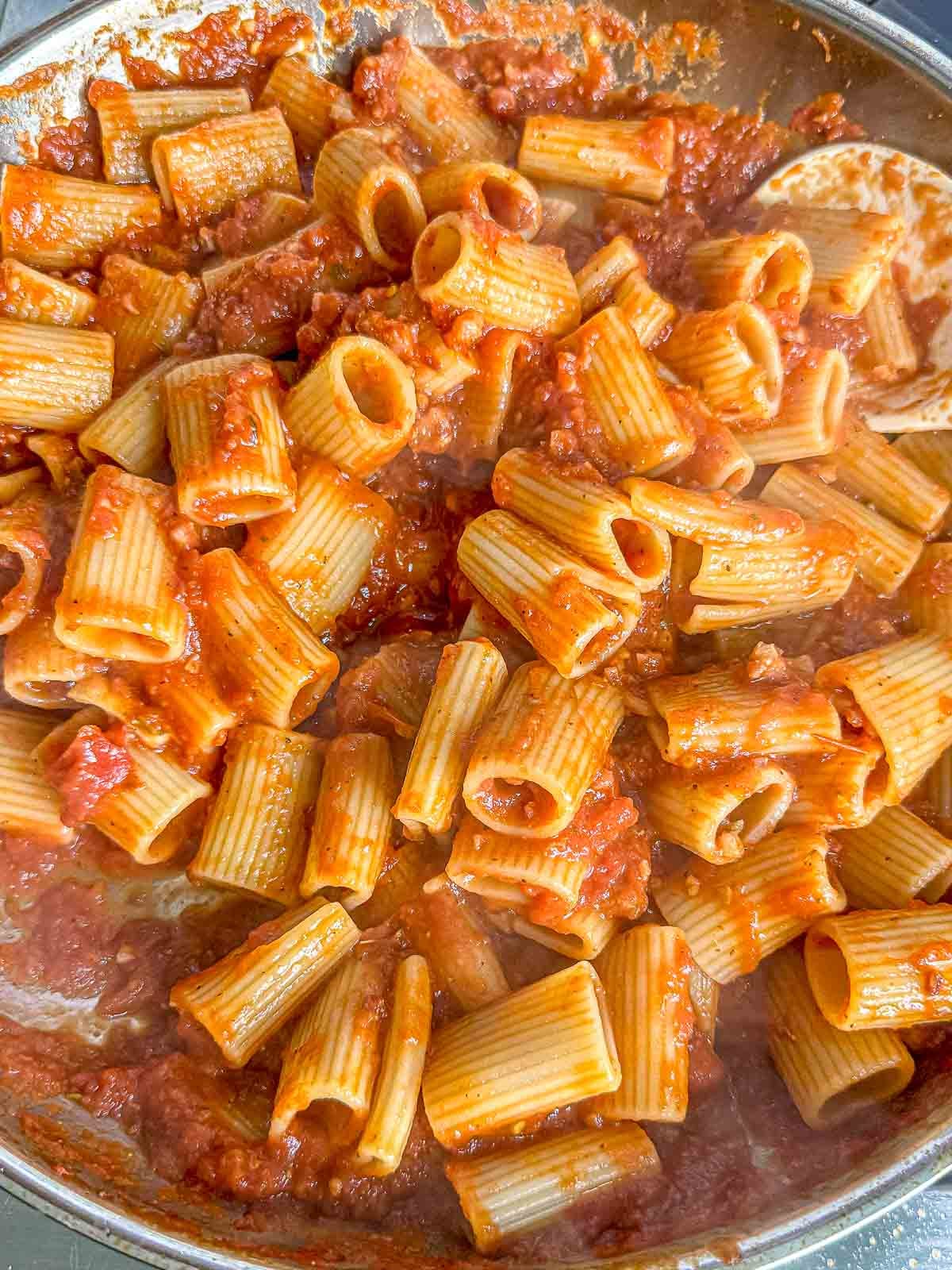 Cooked rigatoni is tossed with spicy tomato sauce and pancetta in a large skillet.