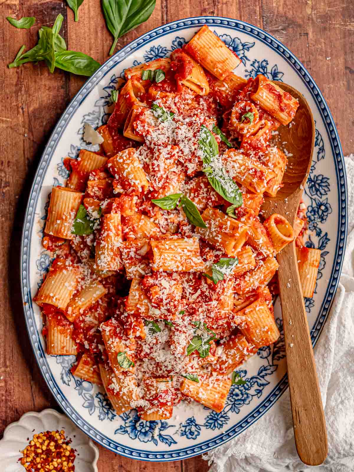 A platter of rigatoni arrabbiata with pancetta is topped with freshly grated Parmesan and basil leaves.