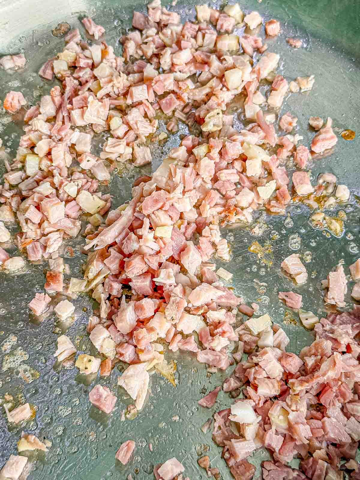 Diced pancetta cooks in a skillet until the fat renders and the edges become golden and crisp.