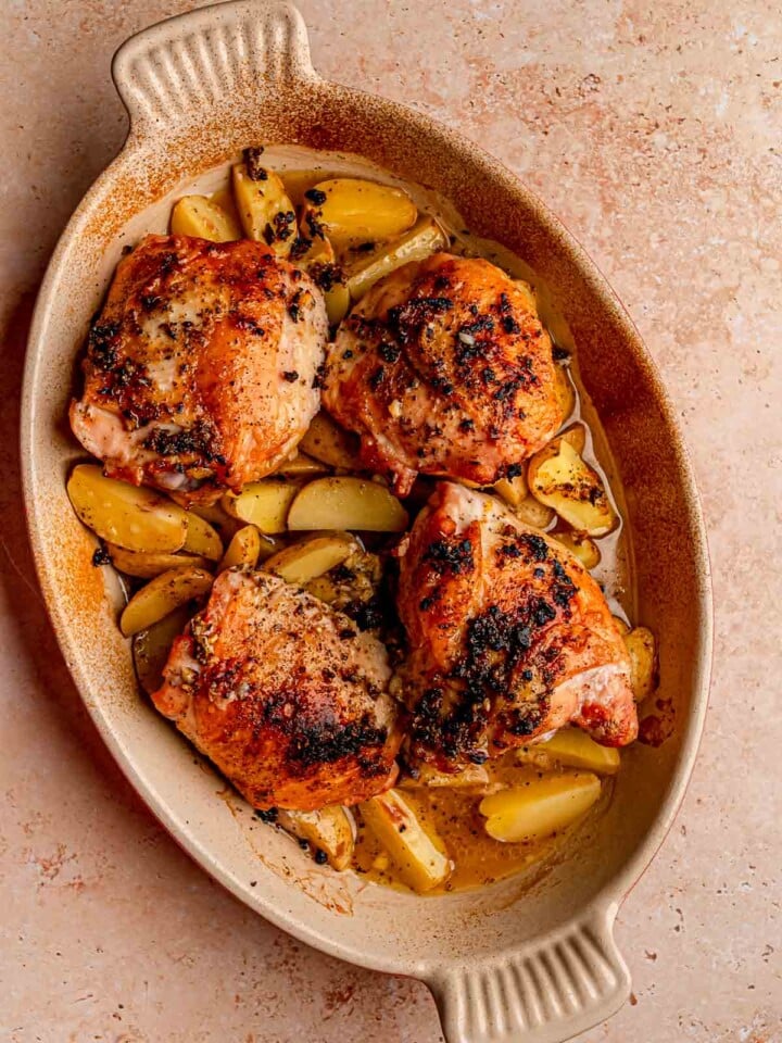Baked chicken thighs and golden potatoes sit in a savory lemon garlic sauce in a casserole dish.