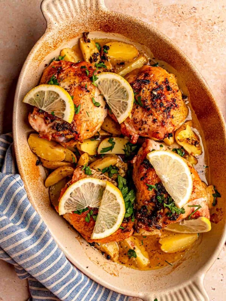 Baked lemon chicken thighs and roasted potatoes are garnished with fresh parsley and lemon slices.