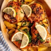 Golden baked chicken thighs and potatoes are topped with fresh parsley and lemon slices in a casserole dish.