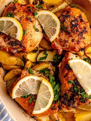 Golden baked chicken thighs and potatoes are topped with fresh parsley and lemon slices in a casserole dish.