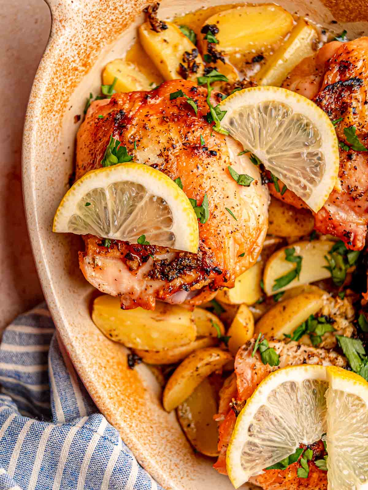 Baked chicken thighs with crispy golden skin are served over lemon garlic potatoes with fresh parsley and lemon.