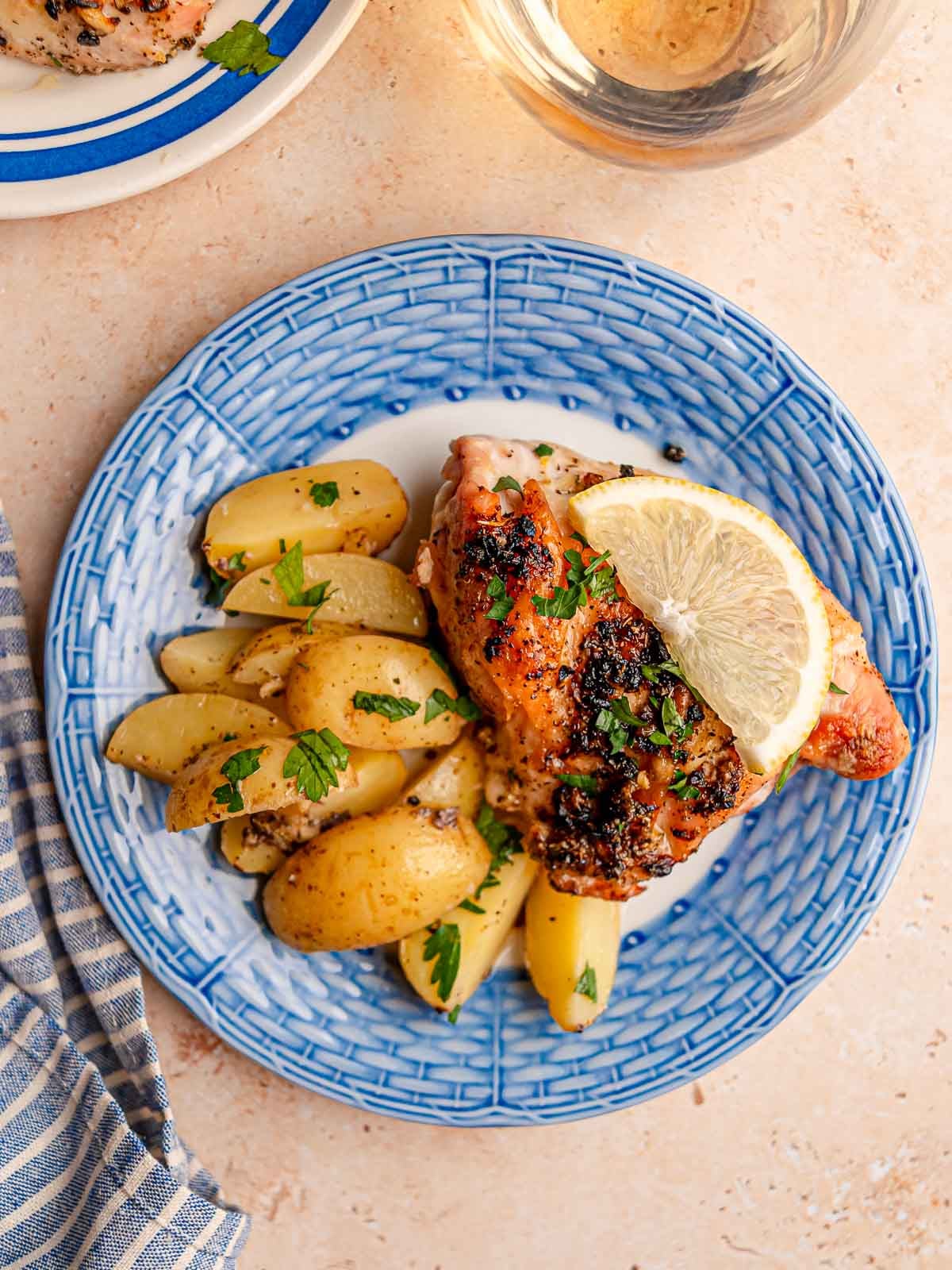 Baked lemon chicken and roasted potatoes are served with parsley and a fresh lemon slice on a blue and white plate.